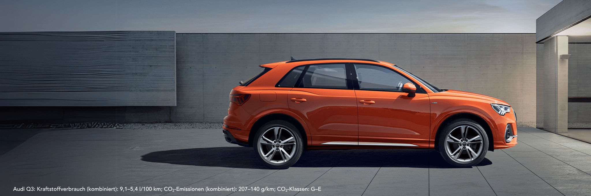 Audi Q3 orange seitlich vor grauer Wand.